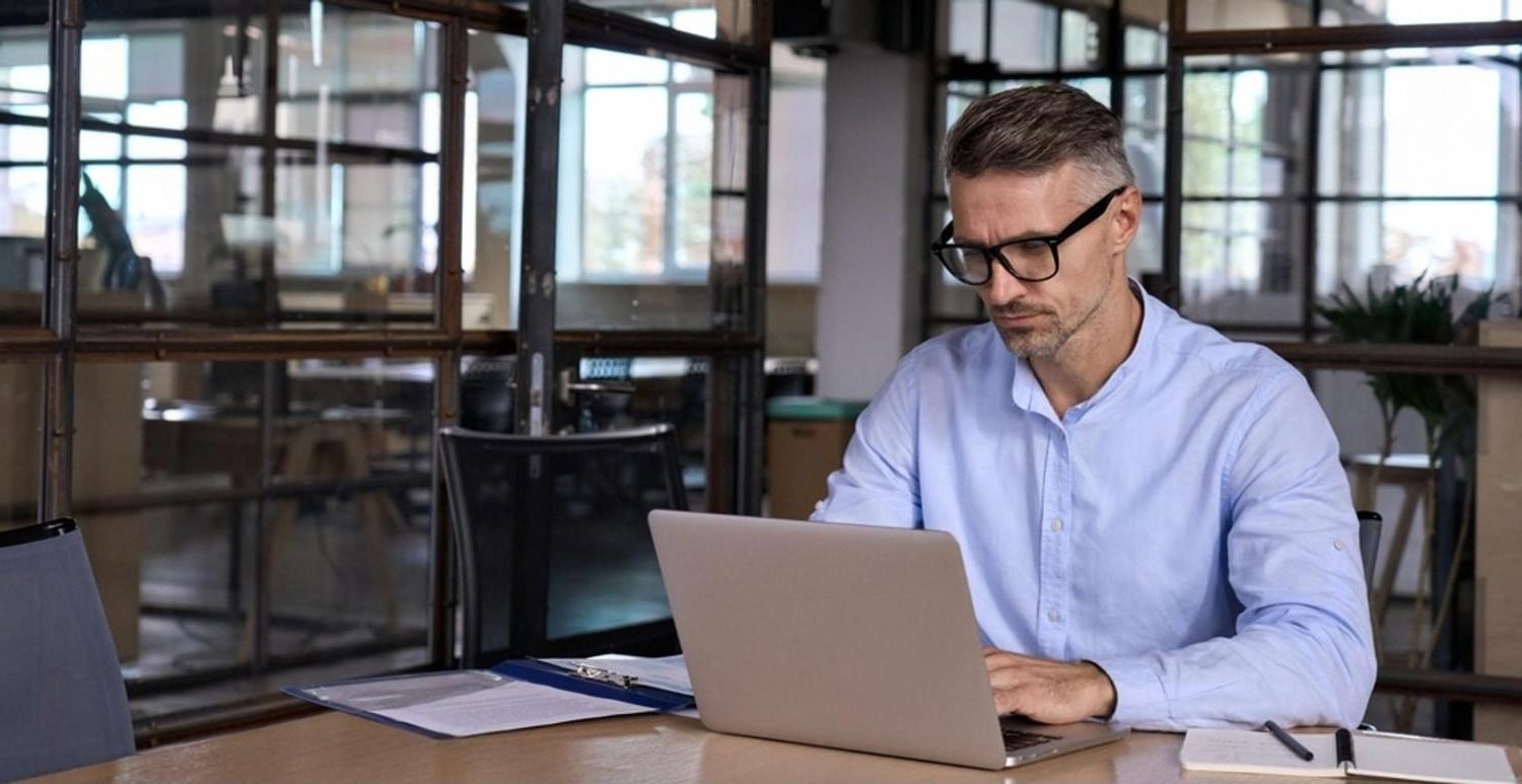 Man in glasses reviewing domain registrar paperwork on a laptop