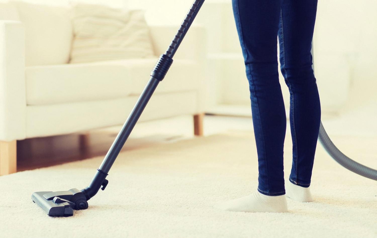 Woman vacuuming a light-coloured carpet in a bright living room